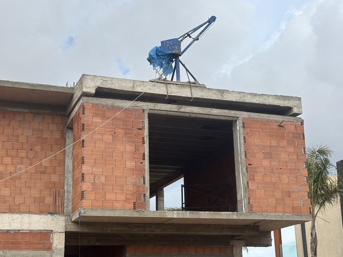 Villa en briques rouges en construction avec grue bleue au sommet et ciel nuageux