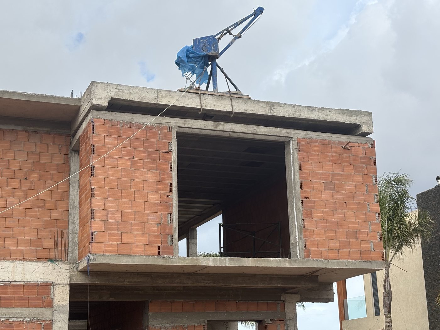 Villa en construction en briques avec grue au sommet et linteaux béton visibles