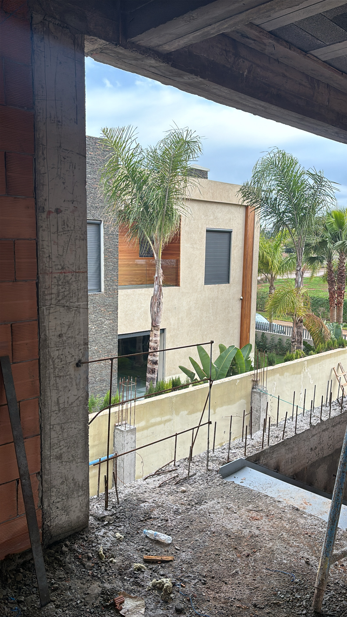 Vue depuis la structure en béton vers les villas voisines avec palmiers et jardin visible