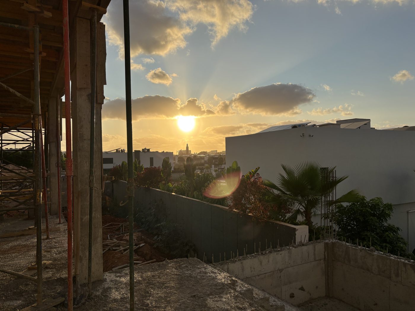 Coucher de soleil doré vu depuis un chantier en cours, avec silhouette de la ville en arrière-plan