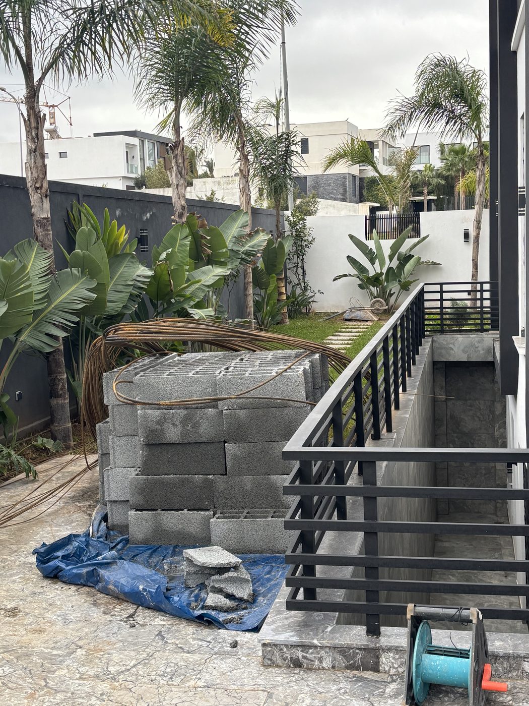 Terrasse villa en cours d'aménagement avec blocs de pierre, palmiers et végétation tropicale